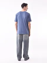 Remera de manga corta color gris topo, corte slim, con cuello redondo y un estampado gráfico en el pecho que combina texto manuscrito con un diseño abstracto en tonos oscuros.