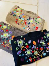 Buzo de punto tejido de lana, con cuello redondo y diseño bordado a mano con motivos florales multicolores.