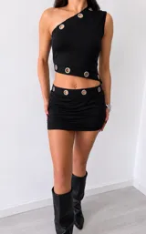Minifalda negra ajustada, con detalle de argollas u ojalillos metálicos plateados dispuestas en la cintura.