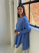 Sweater de punto color celeste, de corte holgado y diseño asimétrico con tajos laterales. Presenta cuello redondo, mangas largas y una costura vertical central en el frente.