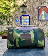 Necessaire de lona con estampado camuflado, detalles en cuero marrón y logo de la marca Sierra Mora en el frente.