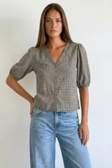 Blusa de algodón con estampado de cuadros vichy en tonos negro y blanco. Presenta escote en V, cierre frontal con botones y mangas cortas abullonadas con terminación elástica.
