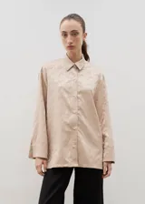 Camisa de corte holgado y diseño clásico, confeccionada en tela satinada con un sutil estampado floral tono sobre tono. Presenta cuello camisero, cierre frontal con botones y mangas largas con puños rectos.