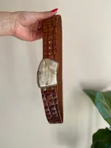 Cinto de cuero color marrón con textura tipo cocodrilo y hebilla plateada con detalle de guampa.