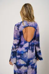 Vestido largo con estampado abstracto en tonos azul, lila y blanco. Tiene cuello mao con abertura en forma de lágrima, mangas largas acampanadas, espalda abierta, tajo frontal y flecos en el ruedo.