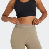 Calza deportiva de tiro alto, color beige, ajustada al cuerpo, con banda elástica en la cintura que lleva el logo de New Balance.