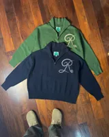 Sweater tejido de algodón en color verde oscuro, con cuello alto y cierre frontal parcial. Presenta un diseño de letra R bordada en color beige en el frente.