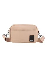 Bandolera de lona impermeable color beige, con diseño compacto, bolsillo frontal con cierre magnético y correa ajustable al tono. Incluye etiqueta de marca en color negro en la parte inferior.