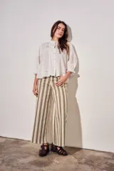 Blusa de algodón peinado color off-white, con cuello mao, cierre frontal de botones, mangas tres cuartos abullonadas con puños con volados, detalles de alforzas y apliques de encaje en el frente y los hombros.