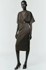 Vestido midi de tejido piqué en color marrón oscuro jaspeado, con escote en pico cruzado y mangas cortas. Presenta detalle de frunces en la cintura y un cinturón integrado con hebilla metálica a contraste.