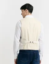 Chaleco de vestir color crudo, con cuello en V y cierre frontal con botones. Posee dos bolsillos ribeteados en la parte inferior y uno tipo ojal en el pecho.