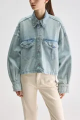 Sobrecamisa oversize de denim celeste con acabado lavado, cuello clásico, cierre frontal con broches metálicos, bolsillos frontales con solapa, mangas largas con puños abotonados y detalle elastizado en el ruedo posterior.
