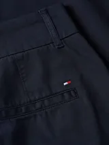 Pantalón chino azul marino de corte slim, con cierre de cremallera y botón, dos bolsillos delanteros de parche y logo de Tommy Hilfiger bordado en la parte trasera.