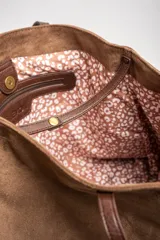 Bolso tipo tote de gran tamaño en color camel, confeccionado en cuero vegano con acabado efecto gamuza. Presenta doble asa larga para llevar al hombro y una placa metálica pequeña con el logo de la marca en el frente.