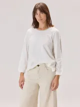 Remera de manga larga color blanco, con cuello redondo y detalle de franja lateral en contraste sobre las mangas. Presenta un corte holgado y cómodo.