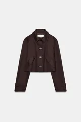 Chaqueta corta de color marrón oscuro, con cuello de solapa, manga larga con trabillas en los puños, bolsillos delanteros con solapa y cierre frontal con botones.