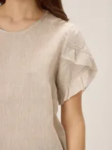 Blusa de lino color blanco, con cuello redondo y mangas cortas adornadas con volados escalonados.