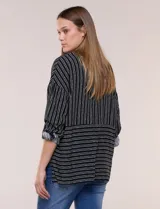 Camisa de rayón negra con patrón de líneas blancas. Presenta cuello camisero, cierre frontal con botones, mangas largas con puños vueltos y un diseño con corte horizontal que alterna líneas verticales en la parte superior y horizontales en la inferior.