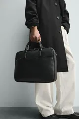 Maletín negro con textura grabada, diseño estructurado y asas de mano. Cuenta con cierre principal de cremallera, bolsillo frontal plano y bolsillo interior para dispositivos electrónicos de hasta 13 pulgadas. Incluye asa de hombro ajustable y extraíble.