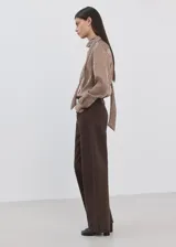 Blusa de manga larga con estampado de rayas verticales en tonos marrones y crema. Presenta un cuello alto con una corbata integrada del mismo tejido y cierre frontal de botones ocultos.