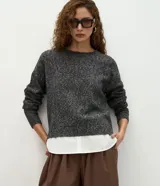 Suéter de punto jaspeado en color gris oscuro, con cuello redondo y mangas largas. Presenta un diseño integrado con una camisa blanca debajo, creando un efecto de capas superpuestas.