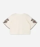 Blusa de corte boxy en color crudo, con cuello redondo y mangas cortas estilo godê. Presenta detalles de bordado floral en tonos marrones en ambas mangas.