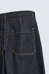 Jeans de denim oscuro, corte ancho (baggy fit) y tiro medio, con costura central girada en el frente de ambas piernas. Presenta pespuntes en color caramelo.