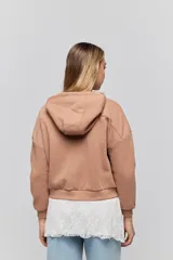 Campera tostada de calce relajado con capucha, cierre frontal, bolsillos laterales y detalles de tachas metálicas.