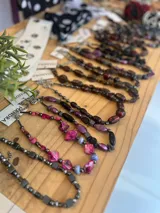 Conjunto de collares de cuentas de diferentes colores y materiales, incluyendo cuentas de piedra, madera y cristal. Los collares tienen cadenas doradas y etiquetas blancas con la marca "MANDRA".