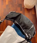 Cartera tipo hobo de cuero sintético color negro, con diseño espacioso y dos bolsillos laterales estilo cargo con cierre. Incluye correa ajustable para el hombro y bolsillo interno.