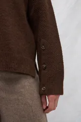 Cárdigan color crema de tejido de punto industrial con escote en V, combinación de puntos y botones decorativos en las mangas.