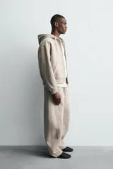 Sudadera tipo hoodie con cierre frontal de cremallera, confeccionada en tejido técnico de algodón con efecto neopreno. Presenta un corte relajado, capucha ajustable con cordones, bolsillos frontales tipo canguro y terminaciones con elástico en puños y ruedo.