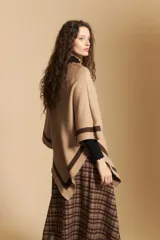 Poncho de silueta amplia y caída fluida, color beige con detalles de líneas en contraste color marrón en los bordes.