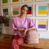 Mochila de diseño compacto en color rosado, confeccionada en símil cuero. Cuenta con un bolsillo frontal con cierre, compartimento principal con apertura superior mediante cierres metálicos, bolsillos laterales y correas regulables para la espalda, además de un asa superior de mano.