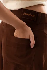 Pantalón de tiro medio con corte súper campana, confeccionado en tela de textura suave. Presenta cierre frontal con cremallera y botón, bolsillos delanteros y traseros, y costuras verticales que definen su estructura.