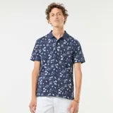 Remera polo azul marino con estampado de palmeras, barcos y paisajes playeros en blanco. De corte clásico y manga corta.