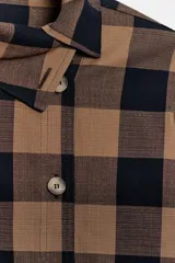 Camisa de manga larga con estampado de cuadros en tonos marrón y negro. Presenta un diseño cruzado con cuello vuelto y cierre frontal de botones, con un corte asimétrico en el bajo.