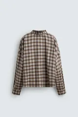 Camisa polo de corte boxy fit confeccionada en tejido de algodón con elasticidad, presenta un estampado de cuadros en tonos marrones, azules y blancos. Cuenta con cuello solapa, cierre frontal de botones, manga larga con puños abotonados y bajo con aberturas laterales.