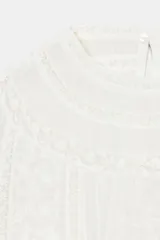 Camisa blanca sin mangas, con cuello redondo y detalle de encaje y bordados florales en el frente.