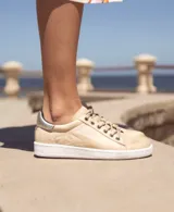 Zapatillas urbanas de cuero metalizado en color dorado, con suela plana cosida en tono tostado y cordones al tono.