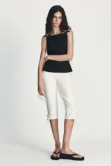 Pantalón capri de tiro alto en color crudo, con detalle de lazos ajustables en los bajos y cierre lateral con cremallera oculta.