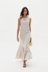 Vestido largo de lino color beige, sin mangas, con cuello redondo y diseño ajustado que se ensancha en la parte inferior con godets que aportan movimiento al ruedo.