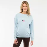 Buzo celeste de muletón con cuello redondo, manga larga y puños de rib. Cuenta con estampa frontal con el texto "San Francisco", una pequeña bandera de Estados Unidos y detalles numéricos.