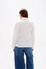 Camisa blanca de algodón con diseño cruzado y anudado lateral, cuello camisero y mangas largas con puños.
