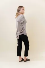 Sweater de tejido liviano con efecto lurex, color beige o gris claro metalizado. Presenta cuello redondo, mangas amplias estilo campana y terminaciones en punto elástico con diseño de cuadros en puños y ruedo.