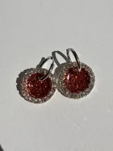 Aros colgantes con forma circular, hechos de resina color lila y borde de strass plateado. El aro es de acero quirúrgico plateado.