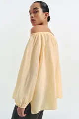 Blusa de lino color amarillo pastel, con escote recto ajustable mediante lazadas, hombros descubiertos y mangas largas abullonadas con puños elásticos.
