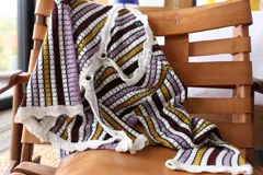 Blusa de tejido de punto calado a rayas horizontales en tonos borgoña, amarillo, lila y blanco. Tiene mangas largas que se ajustan en el codo y se ensanchan hacia el puño.