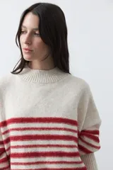 Polera de tejido de punto con diseño a rayas horizontales en color azul marino sobre base beige. Presenta cuello alto, mangas largas con puños acanalados y una silueta relajada.