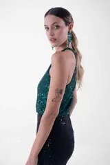 Vestido largo de fiesta con lentejuelas, compuesto por un top verde esmeralda con cuello halter y una falda negra ajustada con abertura lateral.